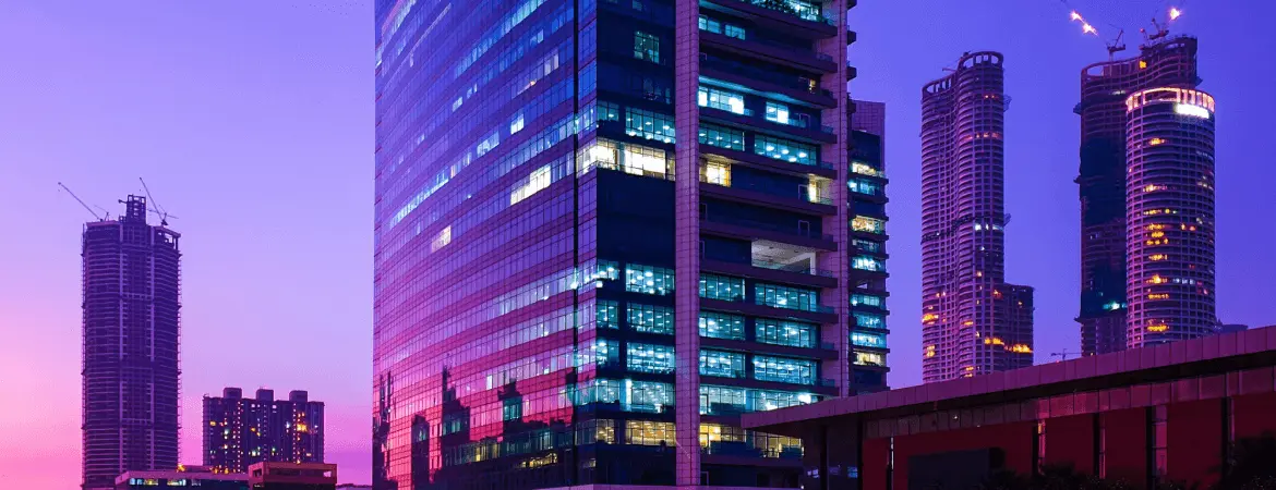 Modern skyline of Faridabad city at sunset with glass office towers, high-rise buildings, and vibrant evening lights.