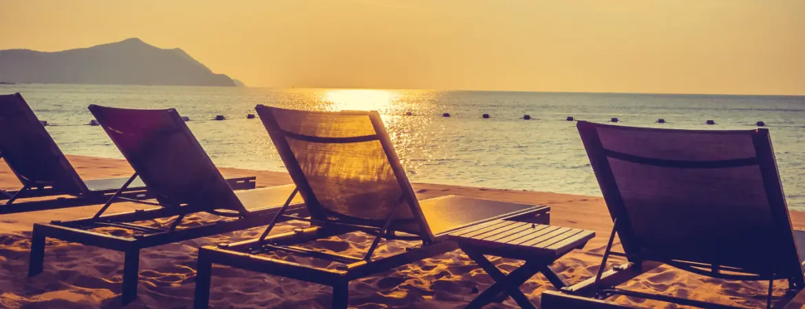 Sunset view at a Goa beach with lounge chairs on sandy shore and golden sunlight reflecting on the sea.